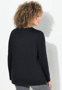 Schwarzes Langarmshirt aus weichem Material mit Rundhalsausschnitt und lockerer Passform, versehen mit seitlichen Schlitzen für zusätzlichen Komfort.