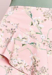 Růžová látka s květinovým vzorem bílých a krémových květin a zelených listů, s volánkovým švem.