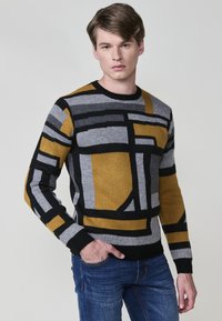 Suéter de punto con patrones geométricos en negro, gris y mostaza. Cuello redondo y puños acanalados, con un acabado de punto texturizado.