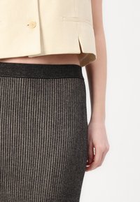 Beige kort kavaj med två framfickor och gula knappar, kombinerad med en svart ribbad stickad kjol med elastisk midja.