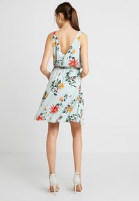 Blommig klänning med V-back, ljusblått tyg, elastisk midja och knälång fåll, med livfulla blommor i röd, gul och grön.