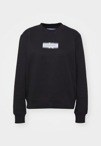 Svart sweatshirt i bomullsmix, med rund halsringning, ribbade muddar och en frampanel med ett logomärke som har text och en stiliserad "K."