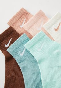 Seis pares de calcetines en varios colores pastel, con el logo de Nike. Los colores incluyen marrón, durazno, verde menta y crema.