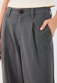 Oglate hlače v ogljeni sivi barvi z gladko teksturo, z enim gumbom, nabranim dizajnom in stranskimi žepi.