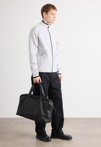 Jachetă gri cu fermoar, cu accente negre, asortată cu pantaloni negri și o geantă din piele neagră. Texturi netede și un design minimalist.