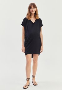 Czarna sukienka ciążowa z miękkiego materiału, z dekoltem w serek, krótkimi rękawami i bocznymi kieszeniami. W połączeniu z czarnymi sandałami na paski.