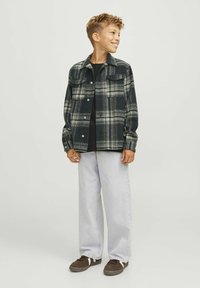 Svart och grön rutigt jacka med knappstängningar, två bröstfickor, i kombination med ljusgrå lösa jeans och mörka sneakers.