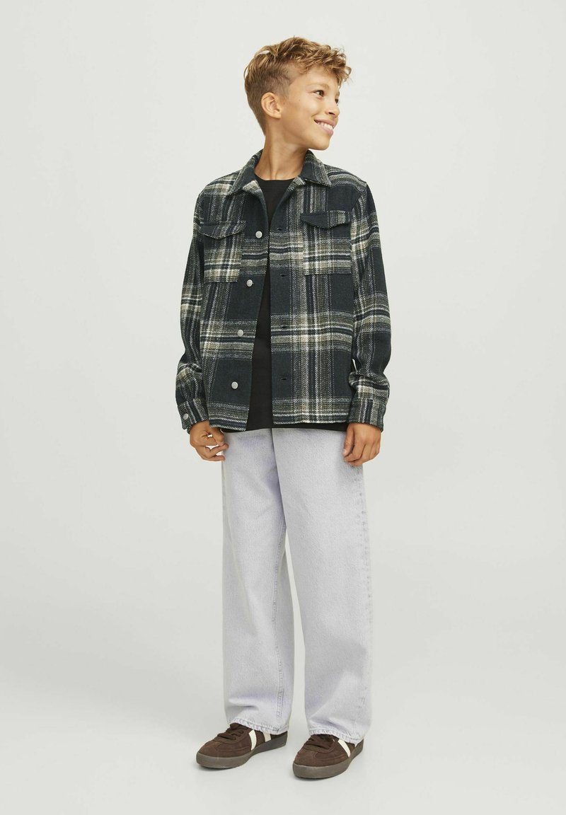 Svart och grön rutigt jacka med knappstängningar, två bröstfickor, i kombination med ljusgrå lösa jeans och mörka sneakers.