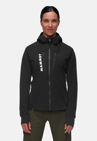Schwarze Softshell-Jacke mit hohem Kragen, Reißverschlusstaschen und einem auffälligen weißen Logo. Sie hat eine sportliche Passform und Daumenlöcher.