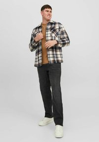 Camisa de franela a cuadros en colores azul marino, crema y marrón, combinada con una camiseta marrón y jeans oscuros. Los zapatos son zapatillas blancas.