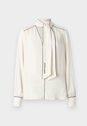 Blusa creme com decote em V, laço destacável e detalhes em preto. Mangas longas com punhos com botões. Acabamento de tecido suave.