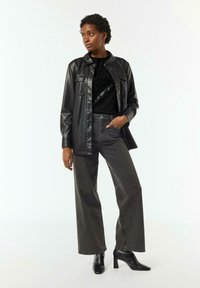 Czarna kurtka z sztucznej skóry noszona na czarnej swetrze z cekinami, w połączeniu z szarymi spodniami o wysokim stanie i czarnymi botkami na obcasie.