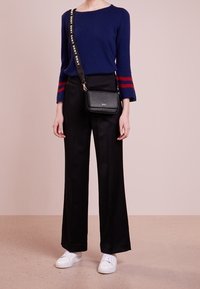 Pullover blu navy con righe rosse sulle maniche, pantaloni neri a gamba larga e sneakers bianche. Borsa a tracolla nera con una fascia decorata.