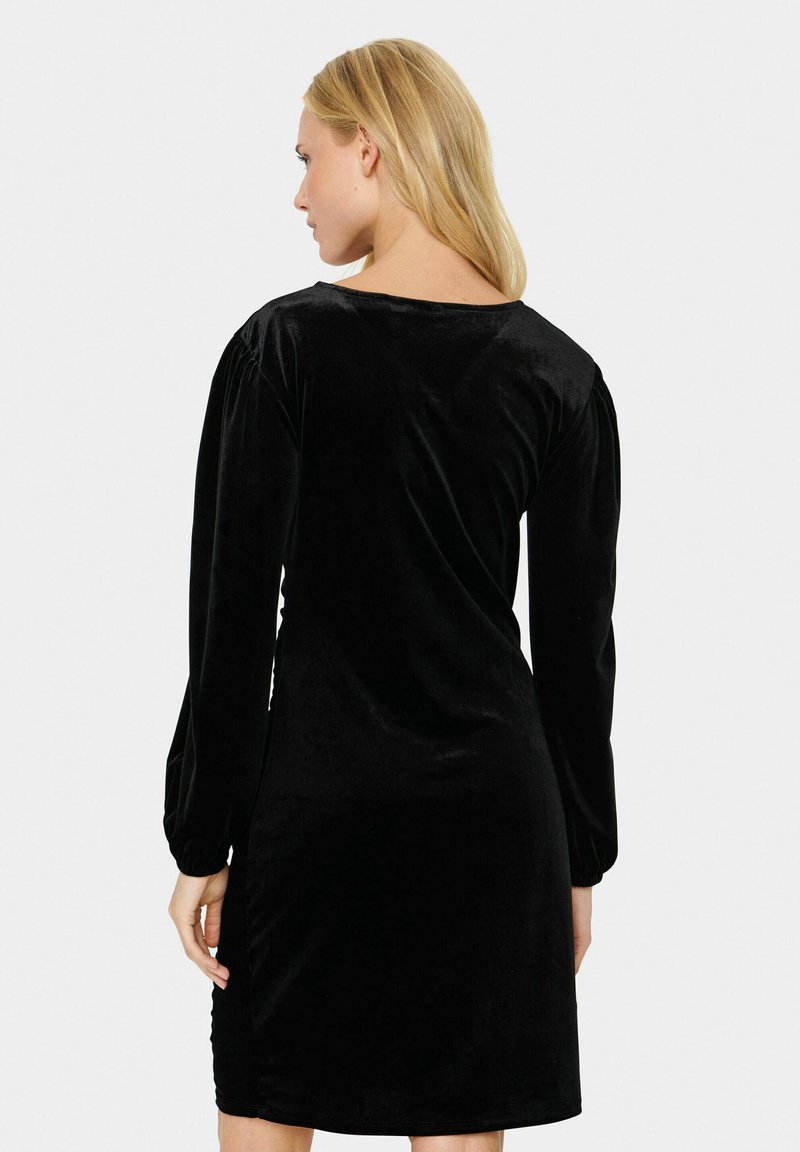 Schwarzes Samtdress mit langen Puffärmeln und tiefem Rückenausschnitt. Glatter Stoff mit einem leichten Glanz, taillierte Silhouette bis zur Mitte des Oberschenkels.