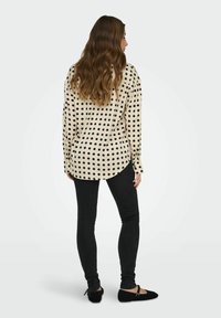 Beżowa bluzka w czarne kropki, z długimi rękawami i zaokrąglonym dołem, w zestawie z czarnymi skinny jeansami i czarnymi balerinami.