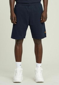Shorts in cotone blu navy con una vita elastica, due tasche laterali e una piccola etichetta arancione vicino all'orlo.
