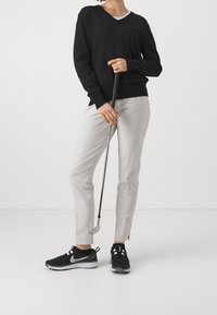 Svart v-ringad tröja i kombination med ljusgrå byxor. Svarta sportskor med vita detaljer. Håller i en golfklubba. Enkel, modern stil.