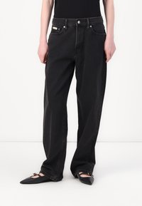 Black denim wide-leg jeans with a high waist, featuring front pockets, a button fly, and a subtle brand tag on the waistband.