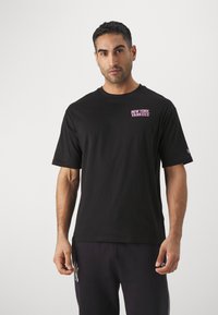 Camiseta de algodón negra con cuello redondo, que presenta un pequeño logo en rosa de "New York Yankees" en el lado izquierdo del pecho y mangas cortas.