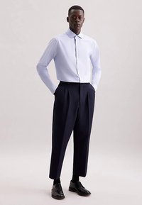 Jasnoniebieska koszula na guziki z długim rękawem, zestawiona z granatowymi zwężanymi spodniami i czarnymi butami. Gładka tkanina, klasyczny kołnierzyk i dopasowany krój.