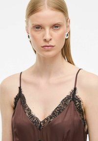 Bruine satijnen slipdress met zwarte kantaccenten. Dunne bandjes en een V-hals ontwerp benadrukken de verfijnde kantdetails aan de randen. Zachte textuur.