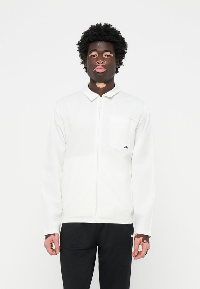 Witte ritsjack met een kraag, voorzien van een enkel borstzakje en logodetail, gecombineerd met zwarte broeken. Glad stoffen textuur.