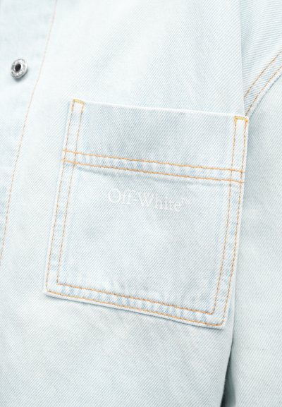 Gaiši zilas denim krekls ar krūtīm kabatu, apšuvumu ar oranžām šuvēm un "Off-White" tekstu, demonstrējot mīkstu tekstūru un ikdienišķu dizainu.