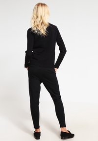 Pull en tricot noir avec un ourlet côtelé, associé à un pantalon noir fuselé. Chaussures plates noires. La texture est lisse et ajustée.