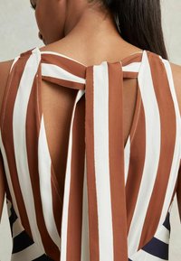 Vestido sin mangas a rayas marrón y blanco que presenta un escote en V en la parte posterior con un lazo atado. La tela parece suave con una ligera textura.