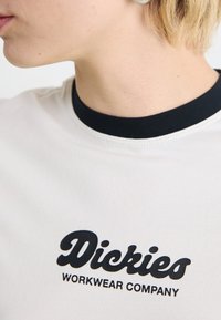 White T-shirt with a contrasting black collar, featuring bold black text "Dickies WORKWEAR COMPANY" in a rounded font.