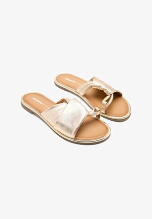 Sandalias deslizantes de color dorado metálico con una textura suave, cintas anchas y una suela flexible. Presentan un diseño fácil de poner y un estilo minimalista.