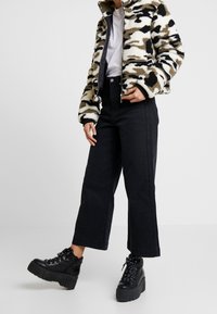 Fleecejacka i beige, svart och olivgrön kamouflage; vit t-shirt; högmidjade svarta jeans; kraftiga svarta snörstövlar med plattform.