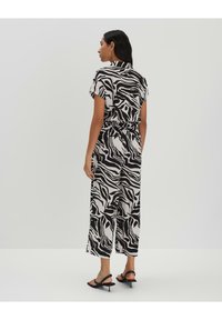 Combinaison à motifs zèbre en noir et blanc avec manches courtes, taille élastique et coupe large ; tissu doux et coupe décontractée.