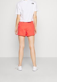 Röda shorts med elastisk midja, tillverkade av lättviktsmaterial. Matchas med en vit kortärmad T-shirt med en svart logotyp på ryggen.