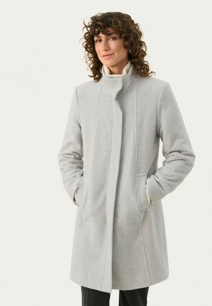 Manteau gris jusqu'aux genoux avec un col montant, des poches latérales et une texture douce. Il présente un design épuré et de légentes coutures verticales.