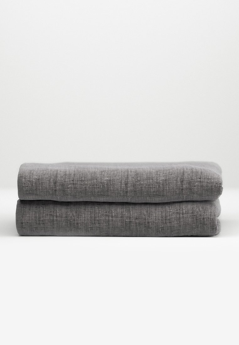 Dwa starannie złożone kawałki szarego lnu ułożone na białej powierzchni na tle jednolitego jasnoszarego tła.