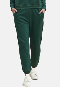 Groene sweatpants van zacht materiaal, met zijzakken, elastische boorden en een relaxed fit. Gemaakt in combinatie met witte sneakers.