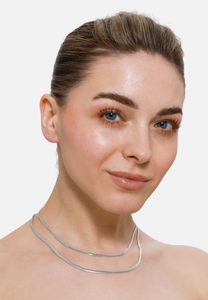 Collier en argent à plusieurs couches avec un design élégant et ondulé. Met en valeur une texture métallique lisse et polie contre un teint de peau neutre.