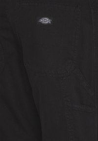 Black denim pants featuring a patch pocket, visible stitching, and a Dickies logo label on the back pocket, with a smooth texture.