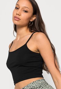 Top cropped preto com alças finas, feito de tecido suave, combinado com uma saia estampada. Apresenta um design ajustado e decote redondo.