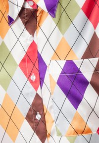 Blusa com padrão argyle multicolorido apresentando diamantes vermelhos, roxos, verdes, laranjas e marrons sobre um fundo branco. Inclui um bolso no peito e botões.