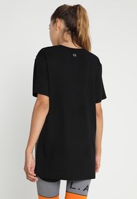 Sort bomulds t-shirt med korte ærmer, en løs pasform og et lille logo på ryggen. Kombineret med mønstrede leggings med orange accenter.