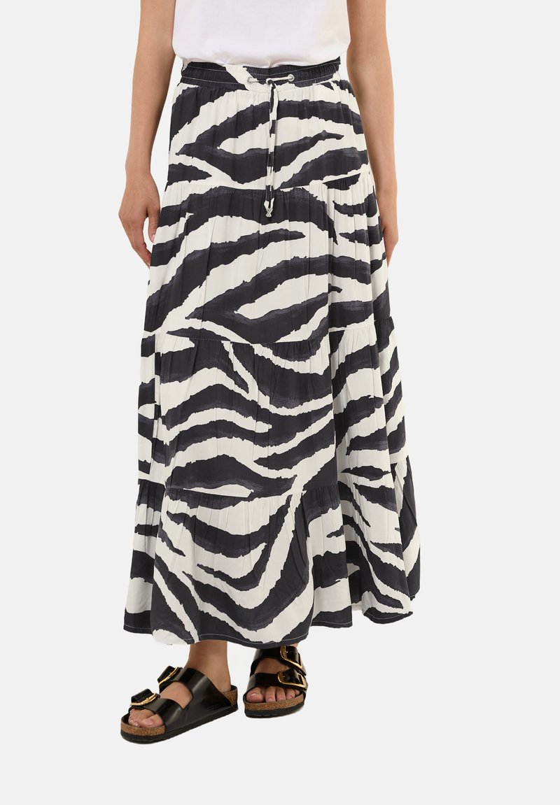 Gonna lunga plisettata con un motivo a righe zebra bianco e nero, caratterizzata da una vita elasticizzata e un cordoncino. Indossata con sandali neri.