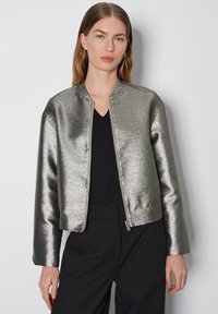 Metalen zilveren bomberjack met een ronde kraag, ritssluiting en lange mouwen. Glad textuur, cropped fit en minimalistisch ontwerp.