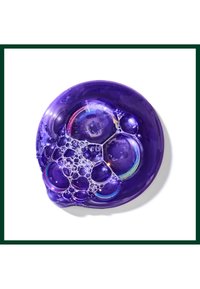 Amas de bulles de savon transparentes aux reflets irisés reposant sur une surface liquide violette sur fond blanc.