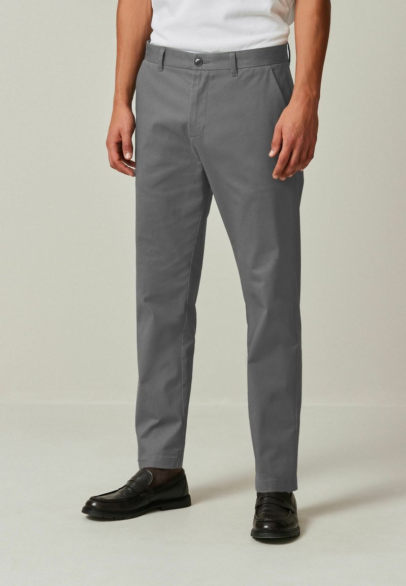 Grå bukser lavet af glat stof, med lynlås og knaplukning samt lige ben-design, parret med sorte loafers.