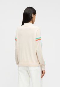 Μπεζ πλεκτό πουλόβερ με ψηλό γιακά, με πολύχρωμες ρίγες στα μανίκια. Απαλή υφή, άνετη εφαρμογή και λεπτομέρεια με ριμπ τελείωμα.