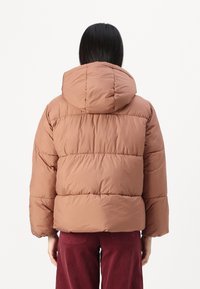 Brun pufferjakke med hette, med quiltede seksjoner og en avslappet passform. Stoffet ser mykt og litt glansfullt ut.