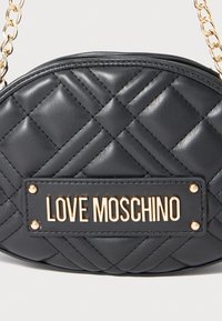 Μαύρη επενδεδυμένη ωοειδής τσάντα χειρός με χρυσή αλυσίδα και χρυσή πλάκα λογότυπου "LOVE MOSCHINO" στο κέντρο μπροστά.