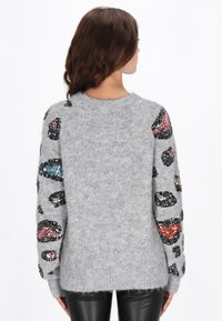 Pulover gri pufos, cu modele colorate din paiete pe mâneci. Guler rotund și tiv cu elastic. Textură moale, croială casual.